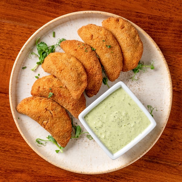 Golden-brown fried empanadas arranged on a plate with a side of creamy green dipping sauce.