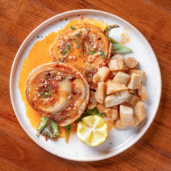 Two crispy pork belly slices with sauce, fried yucca, and a lemon wedge on a white plate.