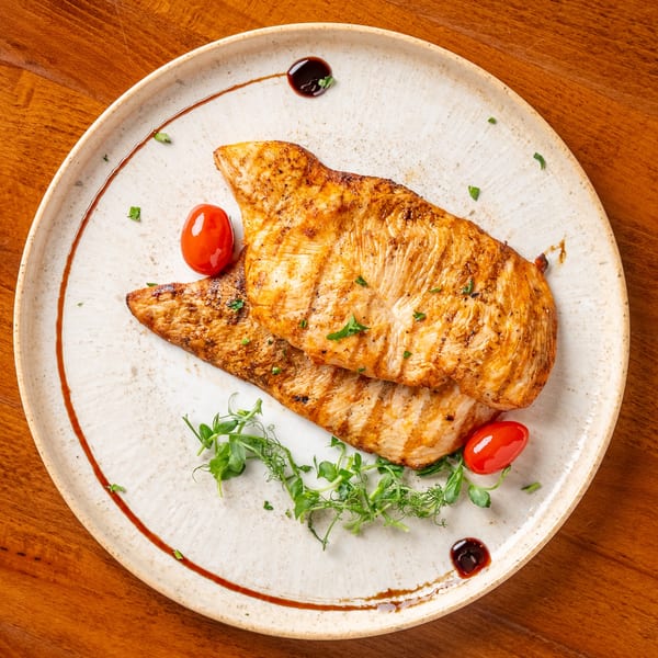 Two grilled chicken breasts with cherry tomatoes and microgreens on a white plate.