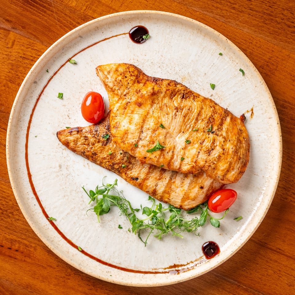 Two grilled chicken breasts with cherry tomatoes and microgreens on a white plate.