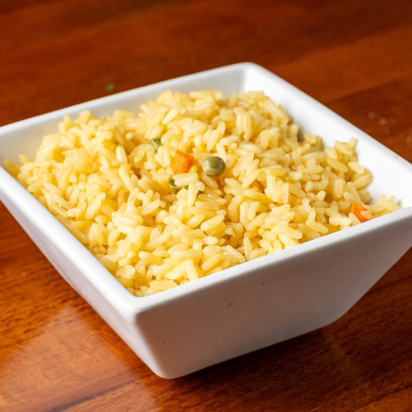 Yellow rice with peas and carrots in a white square bowl on a wooden table.