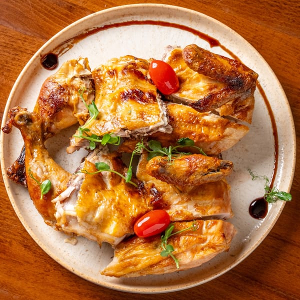 Whole roasted chicken, carved into pieces, garnished with cherry tomatoes and microgreens on a white plate.