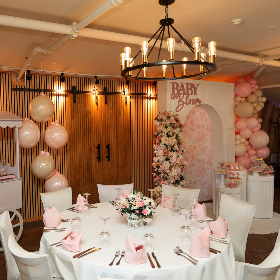 A baby shower setup with a round table, pink and white decor, balloons, and desserts.