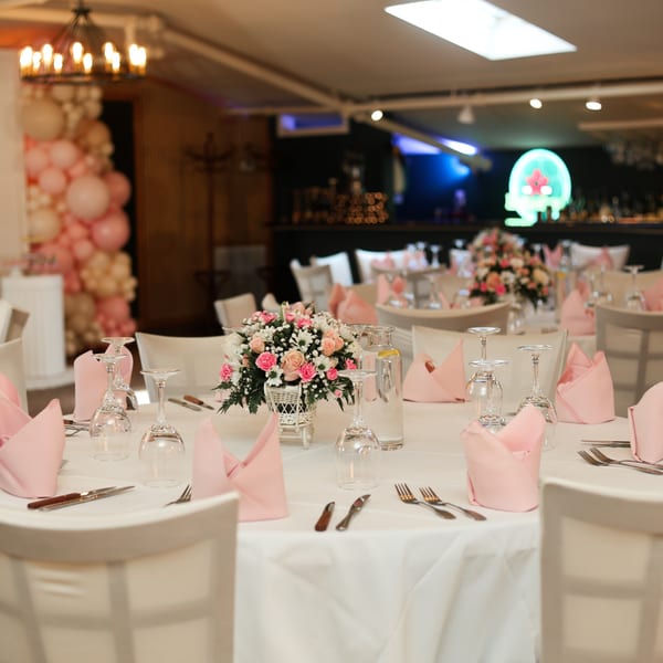 Elegant dining room with white tablecloths, pink napkins, floral centerpieces, and wine glasses.