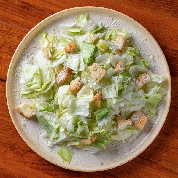 Overhead view of a Caesar salad with lettuce, croutons, and grated cheese on a white plate.